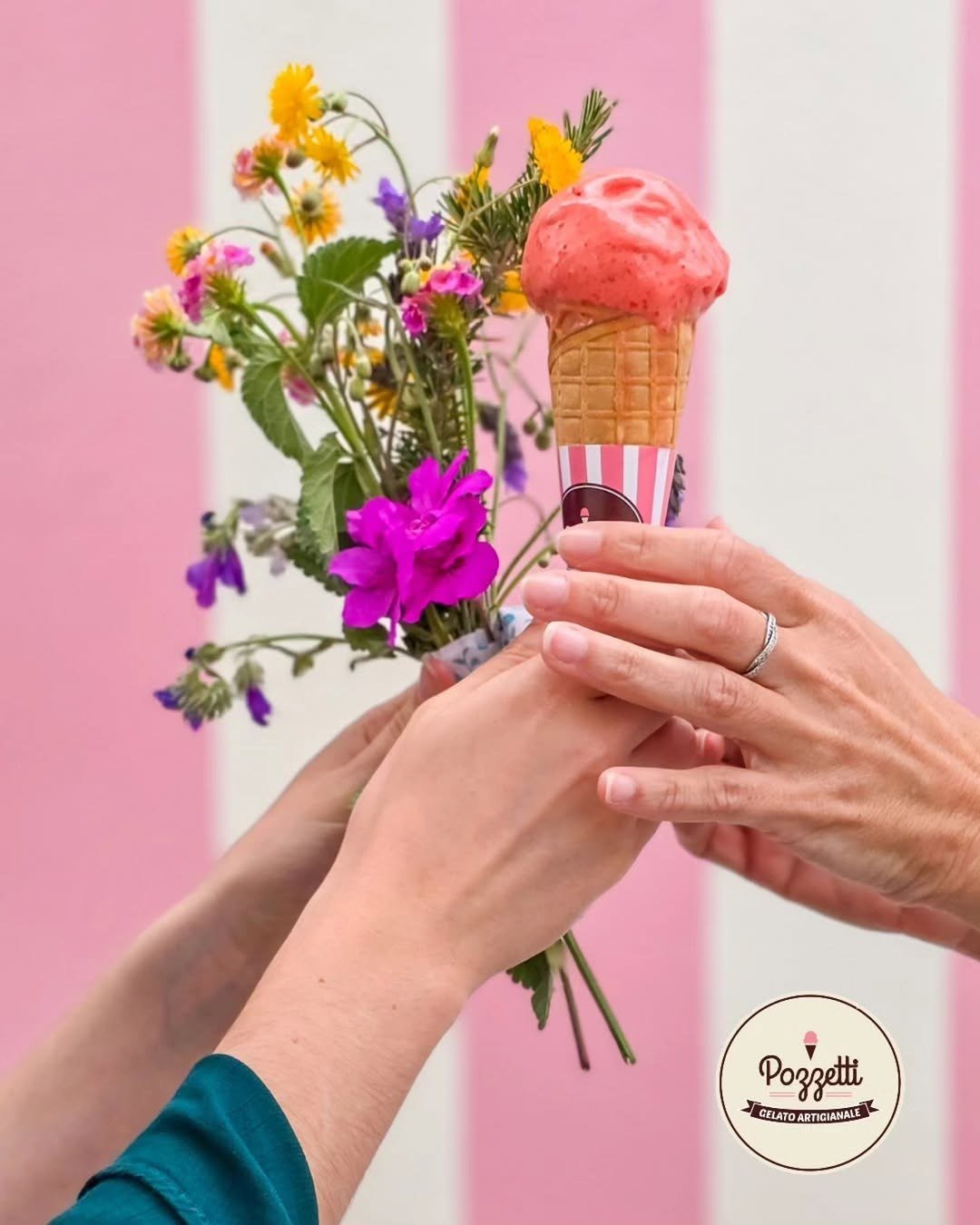 Cone de gelado cor-de-rosa ao lado de um ramo de flores, seguro por duas mãos